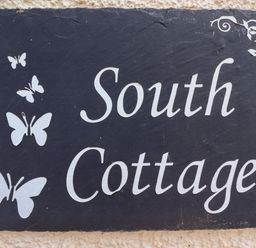 A sign with white butterflies and text South Cottage on a black background at South Cottage Howick Craster