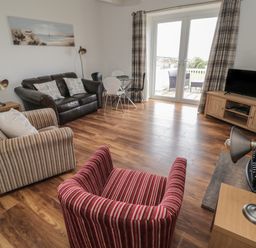 A living room with a striped armchair a leather sofa a striped sofa a glass dining table and chairs a television and patio doors at South Cottage Howick in Craster