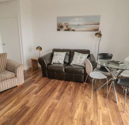 A living room with a striped armchair a black leather sofa with cushions a glass dining table with four chairs two lamps and a painting on the wall at South Cottage Howick in Craster