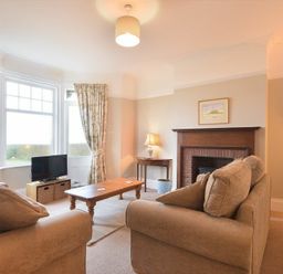 A living room with beige sofas wooden coffee table TV by window and fireplace with artwork at Ty y Mor in Seahouses