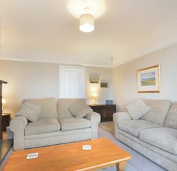 A living room with two beige sofas a wooden coffee table a fireplace and framed pictures on the wall at Ty y Mor in Seahouses