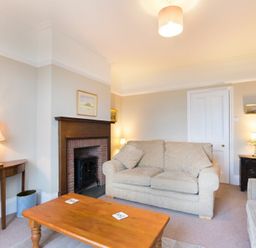 A living room with beige sofas a wooden coffee table lamps and a fireplace at Ty y Mor in Seahouses