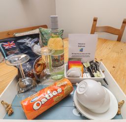 A wooden table with a tray holding a bottle of wine two wine glasses a packet of crisps a pack of oatcakes tea bags and cups at The Boathouse (Seahouses) in Seahouses
