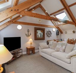 A living room with a beige sofa wooden beams a television and nautical decorations at The Boathouse (Seahouses) in Seahouses