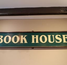A green sign with white letters that reads Book House on a beige wall at The Book House in Warkworth