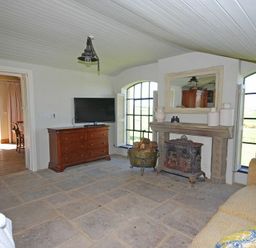A living room with a dresser mounted TV a fireplace and large arched windows at The Huffy House in Alnmouth
