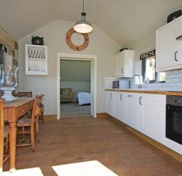 A kitchen with white cabinets wood countertop wooden dining table and chairs and a clock on the wall at The Huffy House in Alnmouth