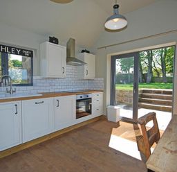 A kitchen with white cabinets wooden countertops and glass doors leading outside at The Huffy House in Alnmouth