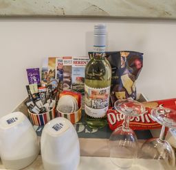 A tray with a bottle of white wine, two inverted glasses, two inverted mugs, packets of tea and coffee, snacks, and brochures at The Little Boathouse in Seahouses