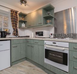 A kitchen with green cabinets a white oven a microwave kettles and a window with a plaid curtain at The Little Boathouse in Seahouses