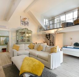 A living room with white sofa yellow cushions a cabinet and a spiral staircase at The Snug in Embleton
