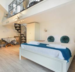 A bedroom with a large bed and blue cushions a spiral staircase table and chairs at The Snug in Embleton