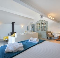 A living area with a bed in the foreground a white sofa a blue cabinet a round table and a television at The Snug in Embleton