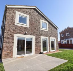 A brick house with white-framed windows and sliding glass door opening to a tiled patio and grass lawn at Tree Corner in Beadnell