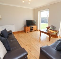 A living room with two black sofas a wooden coffee table and a TV on a wooden stand at Tree Corner in Beadnell