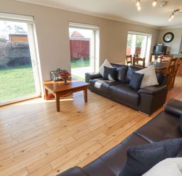 A living room with two dark sofas a wooden coffee table and large windows overlooking a garden at Tree Corner in Beadnell