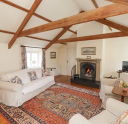 A living room with wooden beams a fireplace sofas a patterned rug and a television at Wynding Down in Bamburgh