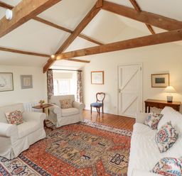 A sitting room with white armchairs a white sofa with patterned cushions wooden beams and a patterned rug at Wynding Down in Bamburgh