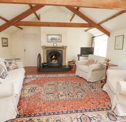 A living room with a fireplace two armchairs a sofa a television and an orange patterned rug at Wynding Down in Bamburgh