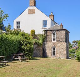 A yard with wooden picnic tables and a stone building with arched windows at The Lookout Embleton