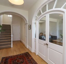 A hallway with wooden flooring a carpet a potted plant on a small wooden table stairs and white double doors leading to a living room at The Lookout (Embleton) in Embleton