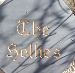 A round stone sign engraved with the words The Sollies mounted on a textured stone wall with shadows and a vine at The Hollies in Bamburgh