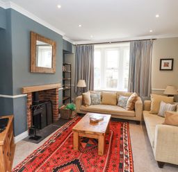 A living room with two beige sofas a wooden coffee table a red patterned rug and a TV on a wooden cabinet at The Hollies in Bamburgh