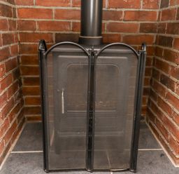 A black wood stove with a mesh fire screen in front set in a brick alcove at The Hollies in Bamburgh