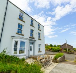 A white multi-story building with a patio table and chairs outside near a road and garden at No6 Sea Lane in Embleton