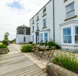 An outdoor patio area with wooden table and chairs next to a white building at No6 Sea Lane in Embleton