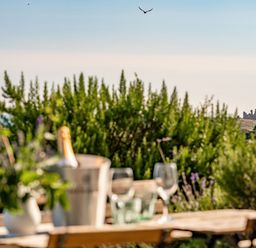 An outdoor table with wine glasses and a bucket with a bottle with greenery and a distant castle by the sea at No6 Sea Lane in Embleton