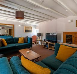 A living room with teal sofas yellow pillows a wooden coffee table a television on a stand and paintings on the wall at The Arches in Bamburgh