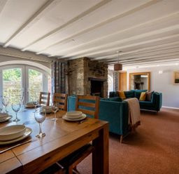 A dining table with dishes and glasses next to a living area with teal sofas and a stone fireplace at The Arches in Bamburgh
