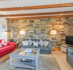 A living room with a red sofa a gray sofa a gray armchair a stone feature wall wooden ceiling beams and a TV at Farne Lookout in Seahouses