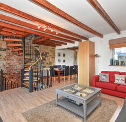A living area with a red sofa and a gray sofa around a coffee table a spiral staircase and a dining table with chairs at Farne Lookout in Seahouses