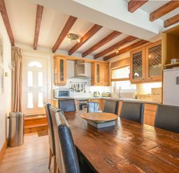A kitchen with wooden dining table and black chairs wooden cabinets and a white door at Farne Lookout in Seahouses