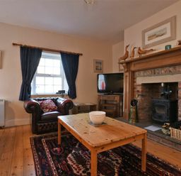A living room with leather armchairs wooden coffee table fireplace and television at Turnstone Cottage Nr Bamburgh