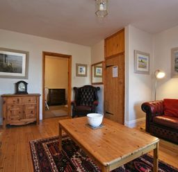 A living room with a wooden coffee table a black leather armchair a red leather sofa with cushions wooden floor and framed pictures at Turnstone Cottage Nr Bamburgh