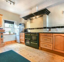 A kitchen with wooden cabinets and black countertop a green stove a refrigerator and a window with a roller blind at Turnstone Cottage Nr Bamburgh