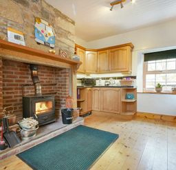 A kitchen with wooden cabinets a wood burning stove and a window at Turnstone Cottage Nr Bamburgh