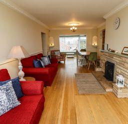 A living room with red sofas a fireplace and a dining table at Barnacle Cove in Beadnell