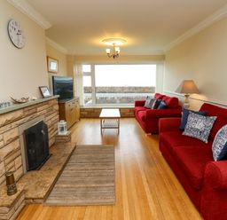 A living room with red sofas wooden floor and large window at Barnacle Cove in Beadnell