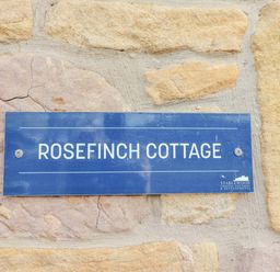 A sign reading Rosefinch Cottage on a stone wall at Rosefinch in Lucker