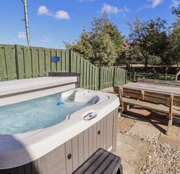 A hot tub with an outdoor table and wooden bench at Rosefinch in Lucker