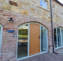 An exterior view of Goldfinch Cottage with a stone wall and an orange front door at Goldfinch in Lucker