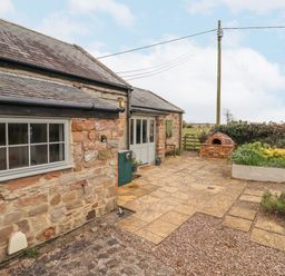 A stone exterior of a cottage with a paved patio garden and outdoor brick oven at Adderstone Cottage in Bamburgh