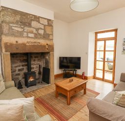 A living room with a stone fireplace wooden coffee table two sofas and a television at Adderstone Cottage in Bamburgh