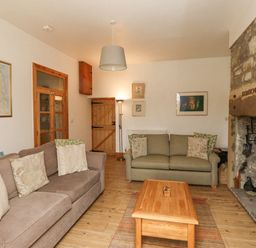 A sitting room with two sofas a wooden coffee table a stone fireplace and a wooden door at Adderstone Cottage in Bamburgh