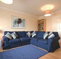 A living room with a blue sectional sofa with striped pillows and a blue rug at Beachcomber Apartment in Bamburgh