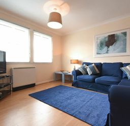 A living room with blue sofas and a blue rug a television on a stand and a framed picture on the wall at Beachcomber Apartment in Bamburgh
